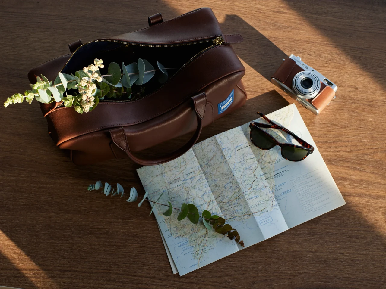 Reise-Flatlay mit Duffelbag, Karte, Sonnenbrille und Kamera auf einem Eichentisch