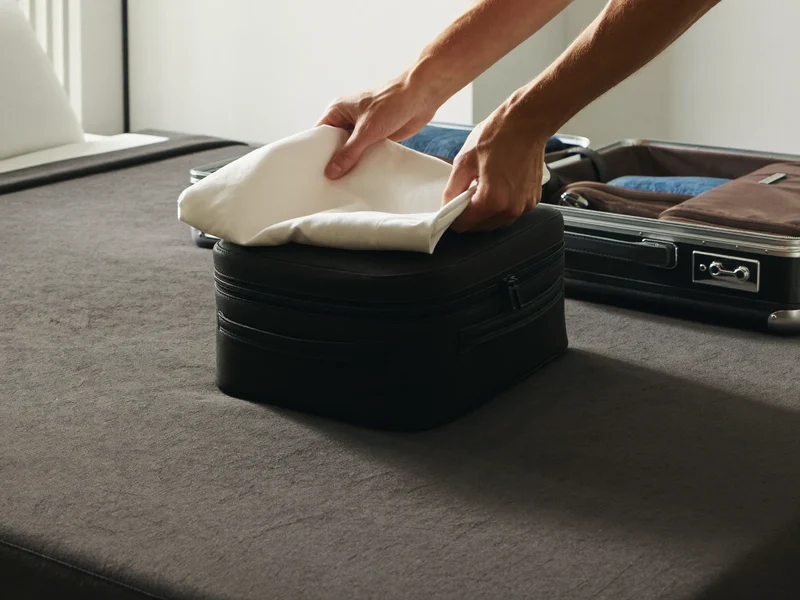 Hände falten ein Hemd in einen Packwürfel neben einem offenen Koffer